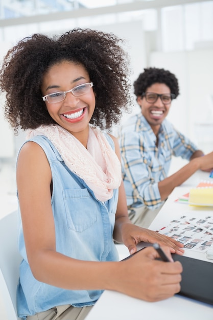 Gelukkig ontwerpteam die bij bureau werken die bij camera glimlachen