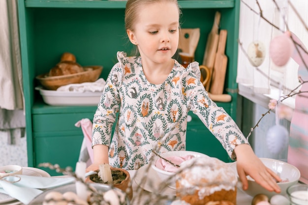 Gelukkig openhartig klein kind van vier jaar oud meisje veel plezier klaar lente paasvakantie thuis keuken helpt haar moeder feestelijke tafel te versieren met paaseieren en bakkerij en snoep voor lunch of diner