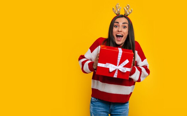 Gelukkig opgewonden jonge brunette vrouw met geschenkdoos in handen geïsoleerd op gele achtergrond