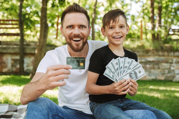 Gelukkig opgewonden jonge vader zit met zijn zoontje geld en creditcard te houden.