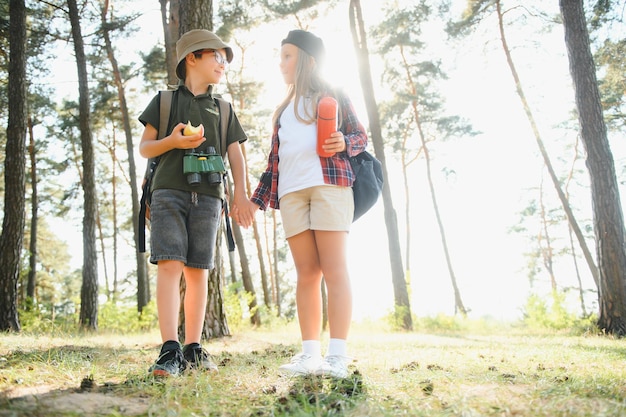 Gelukkig opgewonden schoolkinderen met rugzakken in casual kleding genieten van wandelen in het bos op zonnige herfstdag twee actieve kinderen jongen en meisje samen rennen en spelen tijdens kampeertrip in de natuur