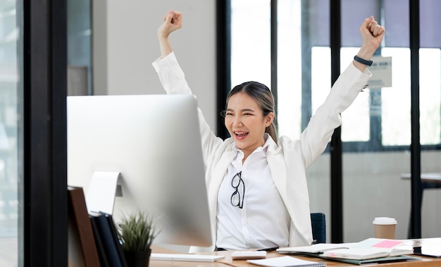 Gelukkig opgewonden succesvolle zakenvrouw zegevieren met desktopcomputer op kantoor