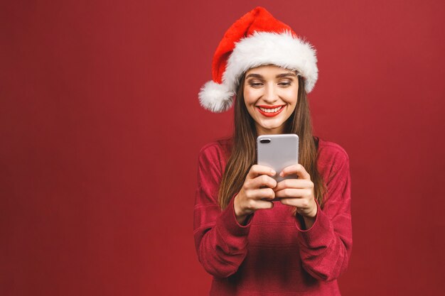 Gelukkig opgewonden vrouw in rode kerstman hoed met mobiele telefoon