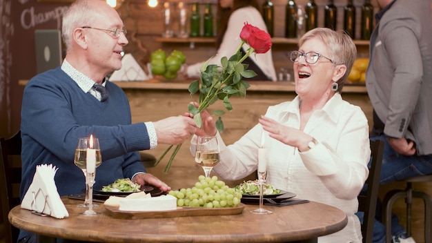 Gelukkig oud paar met rozen tijdens de maaltijd in een restaurant. Pensioen cadeau. Gelukkige oude vrouw. Gelukkig senior man.