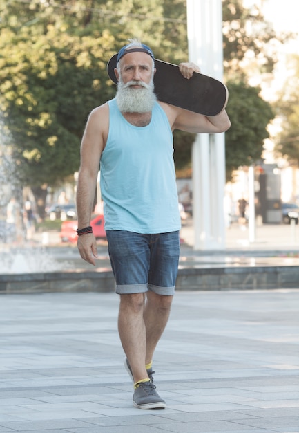 Gelukkig oude man. Het concept van levenstevredenheid. Portret van een positieve grijze man met een skateboard. Winnaar concept.
