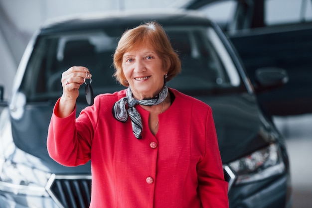 Gelukkig oude vrouw in formele slijtage staat voor moderne witte auto.