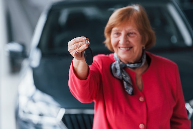 Foto gelukkig oude vrouw in formele slijtage staat voor moderne witte auto.