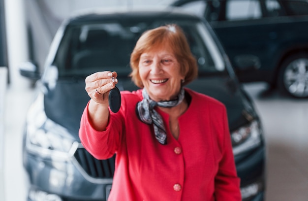 Gelukkig oude vrouw in formele slijtage staat voor moderne witte auto.