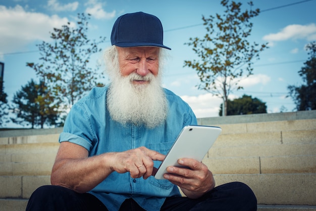 Gelukkig ouderdom. De grijsharige gevorderde oude man de gepensioneerde gebruikt een tablet met een glimlach.