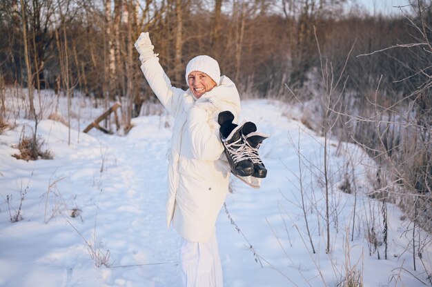 Gelukkig oudere senior rijpe vrouw in witte warme uitloper spelen met ijs-of rolschaatsen in zonnige besneeuwde winter buiten