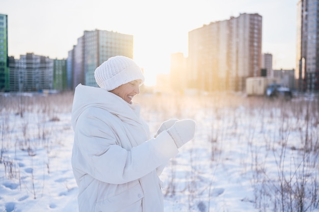 Gelukkig oudere senior rijpe vrouw in witte warme uitloper spelen met sneeuw in zonnige winter buiten