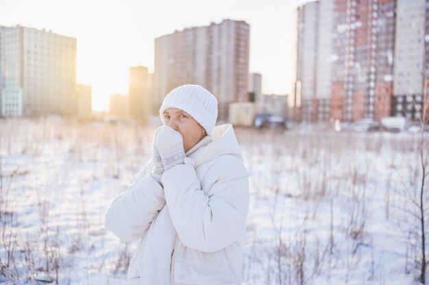 Gelukkig oudere senior rijpe vrouw in witte warme uitloper spelen met sneeuw in zonnige winter buiten