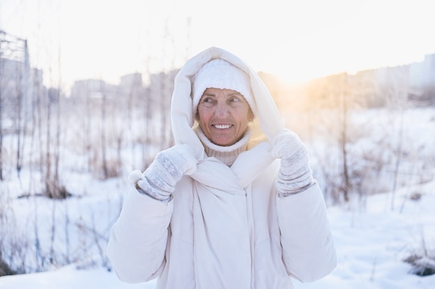 Gelukkig oudere senior rijpe vrouw in witte warme uitloper spelen met sneeuw in zonnige winter buiten