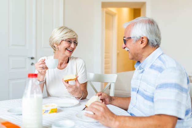 Gelukkig oudere stel dat thuis ontbijt oudere paar dat naar elkaar glimlacht oudere echtpaar dat plezier heeft tijdens het ontbijt eten mensen en gezond eten concept