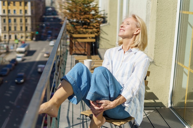 Gelukkig oudere vrouw zittend op terras met kopje koffie en genieten van mooie zonnige ochtend