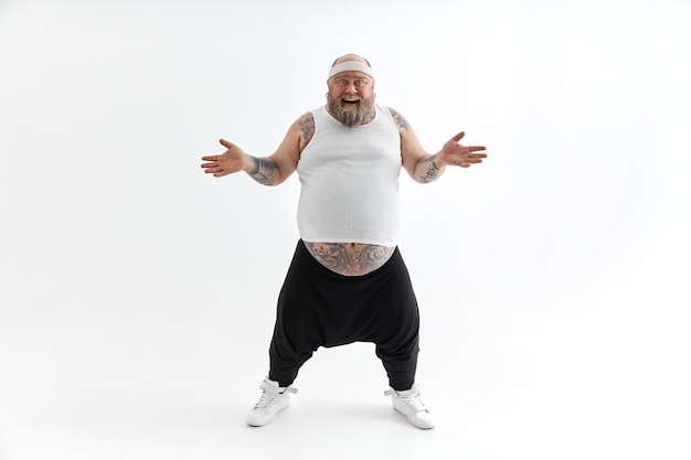 Gelukkig overgewicht man met grote buik en tatoeages in sportkleding die zich voordeed op witte achtergrond
