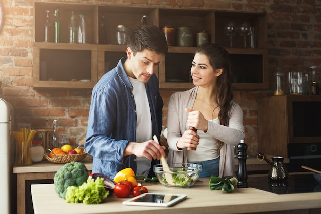 Gelukkig paar dat gezond voedsel samen kookt in hun loftkeuken thuis. Groentesalade bereiden.