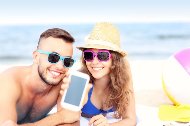 gelukkig paar dat het smartphonescherm toont op het strand