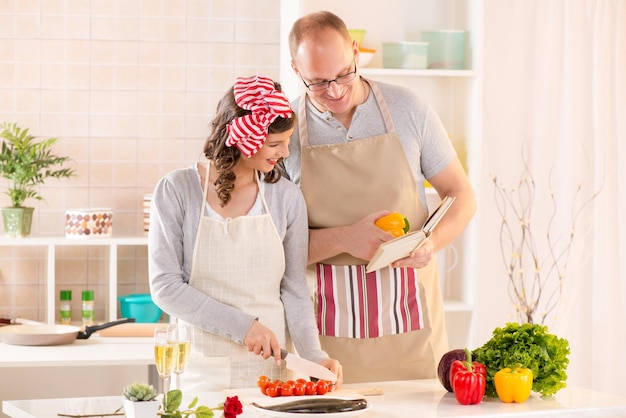 Gelukkig paar dat kookboek leest en voedsel in de keuken bereidt