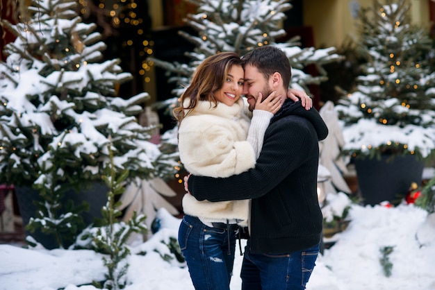 Gelukkig paar die in warme kleren elkaar op kerstmisboom koesteren met lichten. wintervakantie, kerstmis en nieuwjaar.