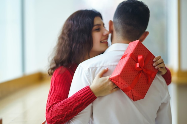 Gelukkig paar met cadeau knuffelen Rode geschenkdoos in de handen van een verliefd paar Valentijnsdag