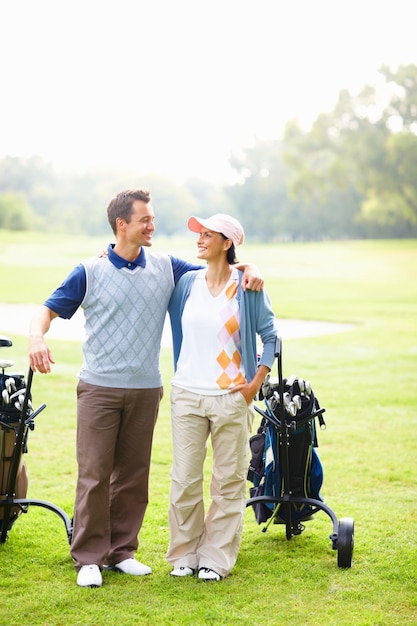 Gelukkig paar op golfbaan Volledige lengte van gelukkig golfend paar met wapens rond glimlachen en elkaar aankijkend