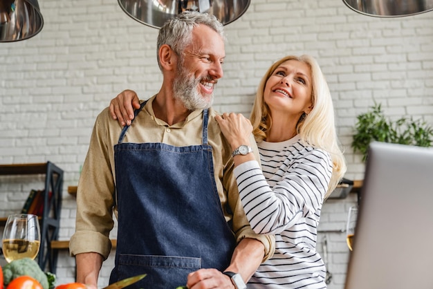 Gelukkig paar van middelbare leeftijd dat plezier heeft tijdens het maken van een diner in de keuken thuis