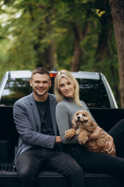 gelukkig paar zit op een auto met een hond in het bos