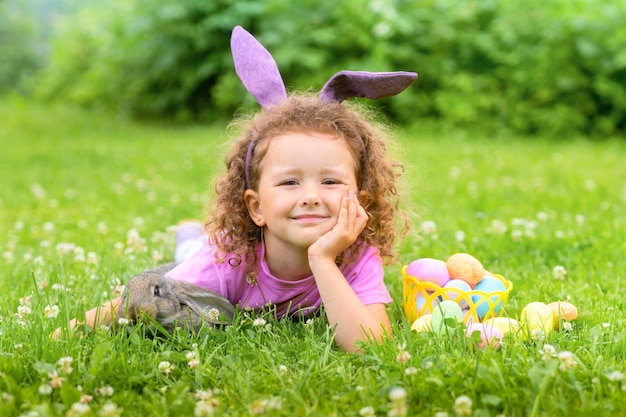 Foto gelukkig paasmeisje en konijnenkonijn op jacht naar kleurrijke eieren op gras voorjaarsvakantie
