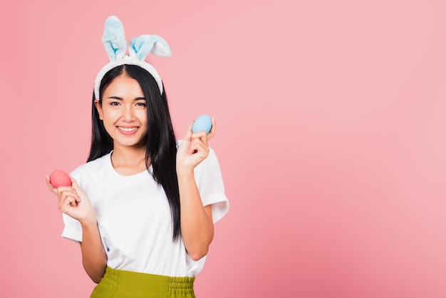 Gelukkig Pasen-concept. Mooie jonge vrouw die lacht met konijnenoren met kleurrijke paaseieren cadeau op handen, portret vrouw kijkend naar camera, studio opname geïsoleerd op roze achtergrond