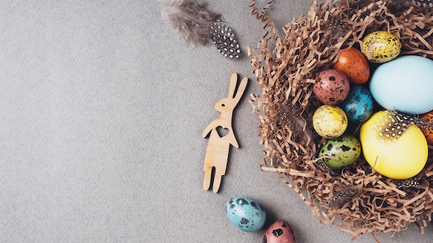 Gelukkig pasen. heldere felicitatie pasen achtergrond. bovenaanzicht, plat lag, kopieer ruimte. kleurrijke paaseieren, konijn en veren in een nest op een grijze achtergrond, close-up.