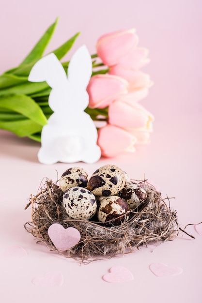 Gelukkig pasen-nest met kwarteleitjes en hart wit konijn en tulpenboeket verticale weergave