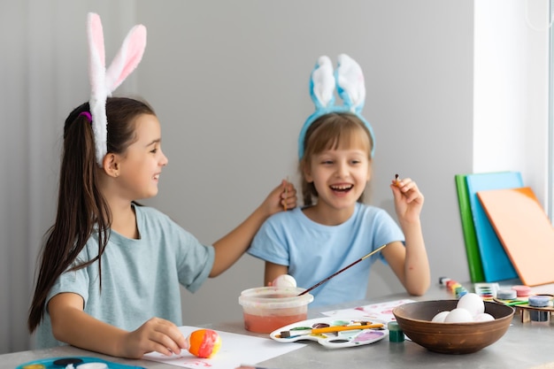 Gelukkig Pasen. Twee zussen paaseieren schilderen. Gelukkige familiekinderen die zich voorbereiden op Pasen. Schattig klein kindmeisje met konijnenoren op Paasdag.