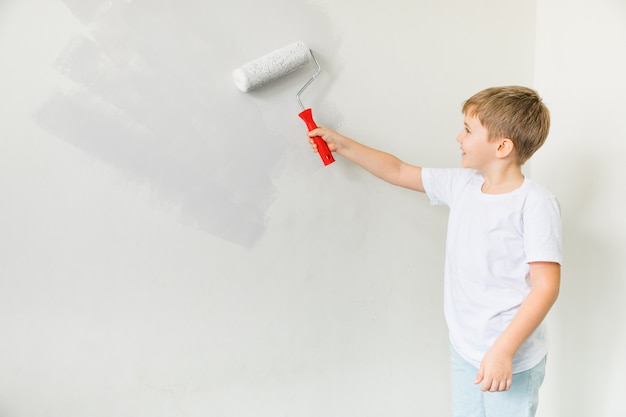 Gelukkig peuter kind schilderij muur. reparatie in appartement. het concept van verhuizen naar een nieuw appartement. schattige kleine jongen schilderij muur in de kamer