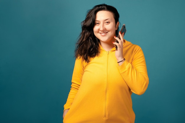 Gelukkig plus size positieve vrouw. Gelukkig lichaam positief concept. Ik hou van mijn lichaam. Aantrekkelijke overgewicht vrouw gekleed in een geel pak leuk poseren voor de camera met telefoon in handen