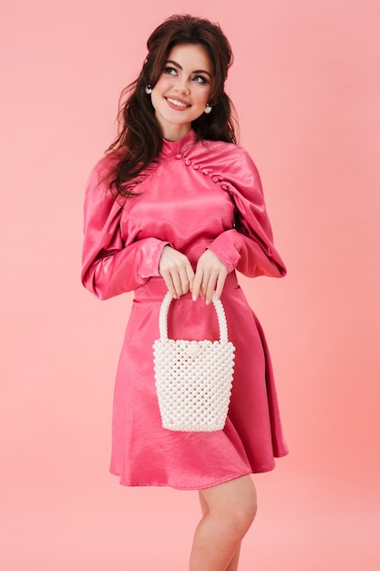 gelukkig positief optimistisch jong glamourmeisje in roze jurk poseren geïsoleerd over roze muur.