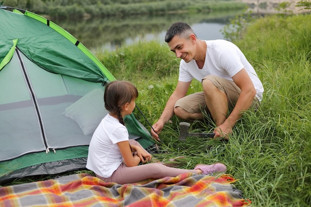 Gelukkig positieve optimistische man en kleine gil dragen witte t-shirts poseren in de buurt van rivier en het opzetten van een tent kamperen in de open lucht genieten van prachtige natuur