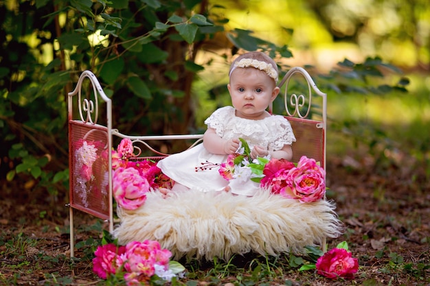 Gelukkig prinsesje babymeisje in bed met roze bloemen buiten in de zomer.