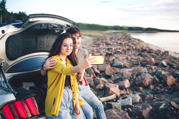 Gelukkig reiziger paar zittend in auto open kofferbak en kijken naar de zonsopgang en Selfie nemen.