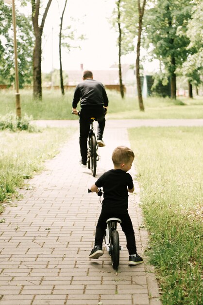 Gelukkig rijdt kleine jongen een fiets met een jonge vader in het park