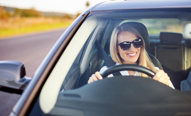 Gelukkig rijpe vrouw in zonnebril en zakelijke slijtage genieten van het besturen van haar moderne auto Weergave van vrouwelijke bestuurder door voorruit Vertrouwen op de weg