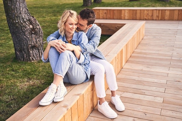 Gelukkig samen. Liefdevolle jonge donkerharige man die zijn aantrekkelijke vrolijke blonde vriendin in zijn armen vouwt