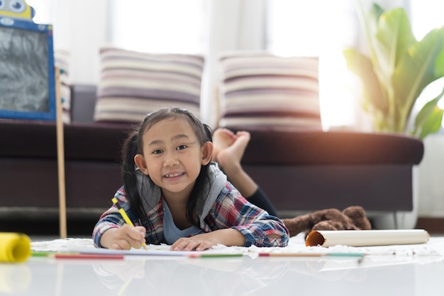 Gelukkig schattig Aziatisch meisje tekenen met kleurrijke potloden terwijl ze thuis op de vloer liggen