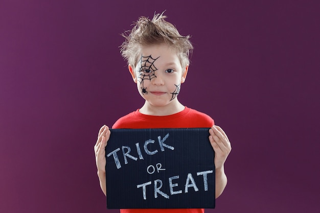 Gelukkig schattig kind met Halloween-make-up, met een schoolbord met de tekst: Trick or Treat. Halloween-concept.