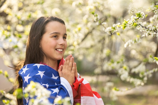 Gelukkig schattig klein meisje glimlachend en zwaaiende Amerikaanse vlag buiten. Glimlachend kind dat 4 juli viert - Onafhankelijkheidsdag