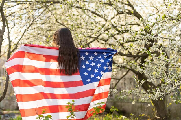 Gelukkig schattig klein meisje glimlachend en zwaaiende Amerikaanse vlag buiten. Glimlachend kind dat 4 juli viert - Onafhankelijkheidsdag