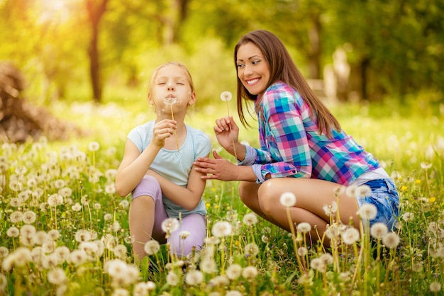 Gelukkig schattig klein meisje waait paardebloem met moeder in het park.