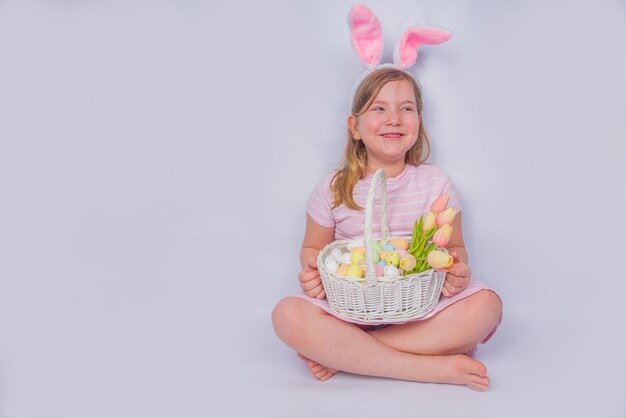 Gelukkig schattig meisje met konijnenoren. Pasen wenskaart achtergrond. met paaseieren en lentebloem in mand