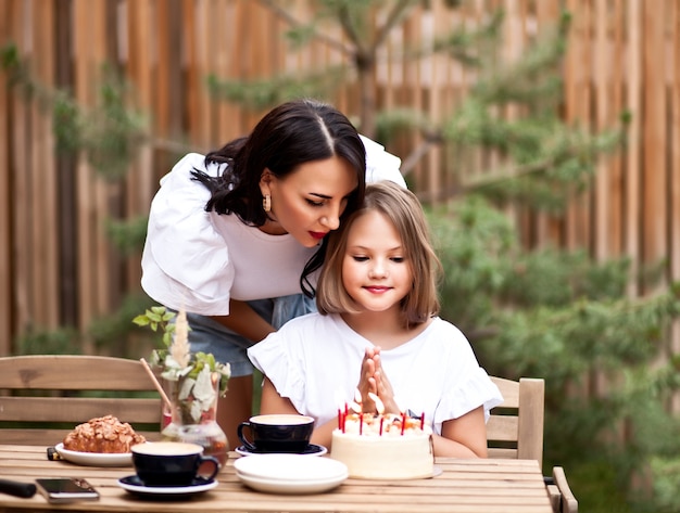 Gelukkig schattig meisje met moeder vieren met verjaardagstaart in café terras. 10-jarige verjaardag vieren.