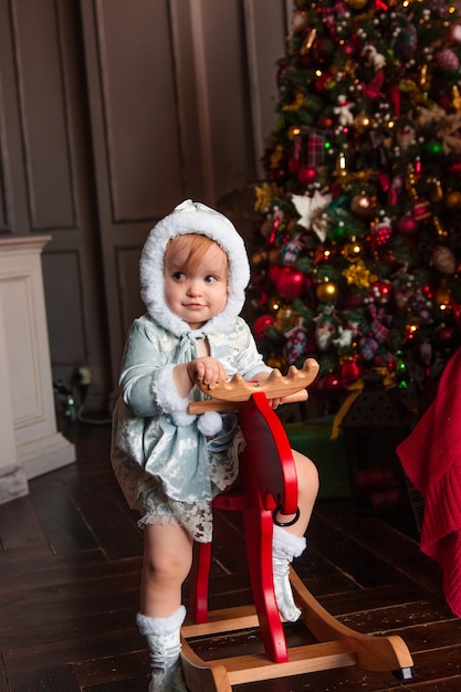 Gelukkig schattig mooi klein meisje zit op een vintage houten chairdeer met kerstversiering